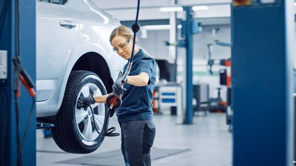 Blond Female Mechanic is Checing the Tire Pressure in a Wheel of a Vehicle. Empowering Woman Works in a Modern Clean Car Service. Specialists Inflates the Wheel After Fixing a Component on a Vehicle. - Foto, imagen