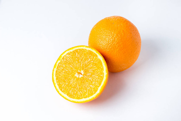 Narancsok fehér háttérrel. Az egyik narancs egész, a másik ketté van vágva. Trópusi gyümölcsök - Fotó, kép