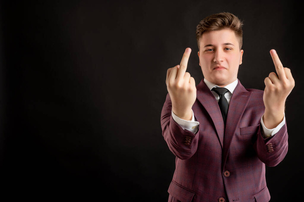 Law student with blond hair dressed in burgundy jacket, white shirt and black tie showing double fuck you posing on isolated black background with copy space advertising area - Fotó, kép