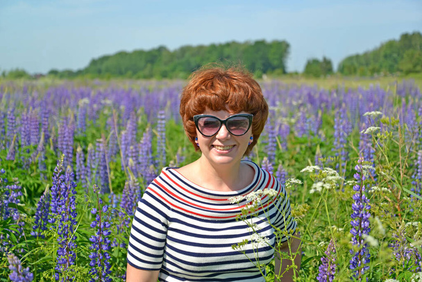 Portrait of a middle-aged woman in sunglasses among blooming lupins - Fotografie, Obrázek