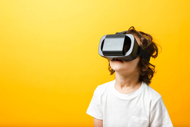 Close-up van kleine jongen in virtual reality headset. Jongen draagt virtual reality bril wit tshirt op gele achtergrond - Foto, afbeelding