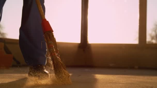 ÁNGULO BAJO: Contratista barriendo el suelo sucio con una escoba de paja al atardecer. - Metraje, vídeo