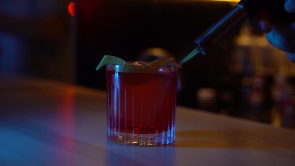 Barman steekt sinaasappelschil in brand op Americano cocktail in een bar met blauw licht. Barthender maakt alcohol cocktail americano in de bar - Video