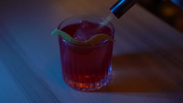Barman sets fire to orange peel on Americano cocktail in a bar with blue light. Barthender makes alcohol cocktail americano in the bar - Felvétel, videó