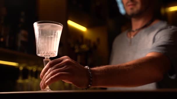 Barista scorre un bicchiere su una gamba alta con scintille e un grande pezzo di ghiaccio all'interno di un cocktail alcolico francese 75. Barman fare cocktail con gin al bar. - Filmati, video