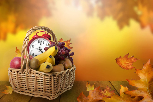 Fruit basket with alarm clock, autumn leaves background, daylight saving time and harvesting concept - Photo, Image