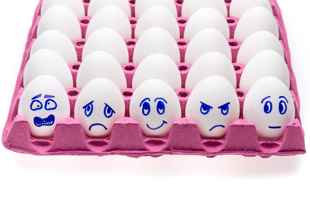 Grappige eieren. Een vrolijk lachend ei tussen trieste, boze en jaloerse menigte eieren geïsoleerd op witte achtergrond - Foto, afbeelding