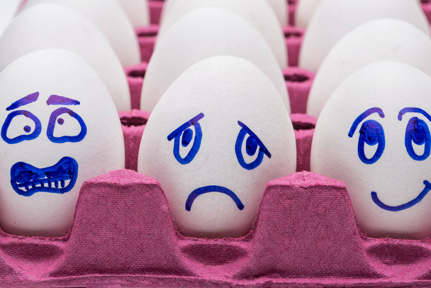 Grappige eieren. Een vrolijk lachend ei tussen trieste, boze en jaloerse menigte eieren geïsoleerd op witte achtergrond - Foto, afbeelding