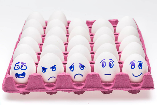 Śmieszne jajka. Jedno szczęśliwe uśmiechnięte jajko pośród smutnego, wściekłego i zazdrosnego tłumu jaj odizolowanych na białym tle - Zdjęcie, obraz