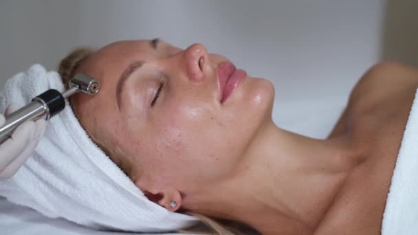 Kosmetologia. Kobieta w klinice otrzymuje stymulację elektrycznego leczenia twarzy. Zbliżenie młodej kobiecej twarzy podczas terapii mikroprądem.      - Materiał filmowy, wideo