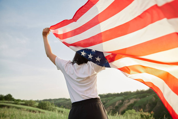 Le 4 juillet. Le 4 juillet. Femme américaine avec le drapeau national américain contre un beau monument. Jour de l'indépendance. Belle lumière du coucher du soleil. Vacances patriotiques, respect de la démocratie et concept de respect des anciens combattants - Photo, image