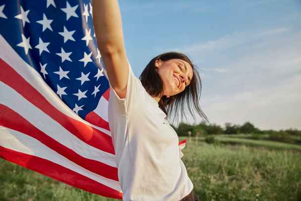7月4日。7月4日。美しいランドマークに対する国旗を持つアメリカ人女性。独立記念日。美しい夕日の光。愛国的な休日、民主主義の尊重とベテランの尊敬の概念 - 写真・画像