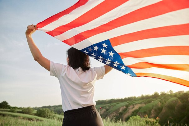 Il 4 luglio. Il 4 luglio. Donna americana con la bandiera nazionale americana contro un bellissimo punto di riferimento. Il giorno dell'indipendenza. Bella luce del tramonto. Vacanza patriottica, rispetto della democrazia e concetto di rispetto dei veterani - Foto, immagini