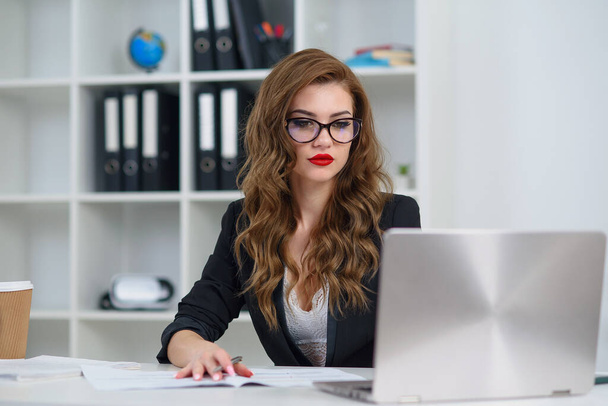 Successful businesswoman at official clothes sitting in cozy bright office and working with laptop computer. Concept of experienced company manager. - Фото, зображення