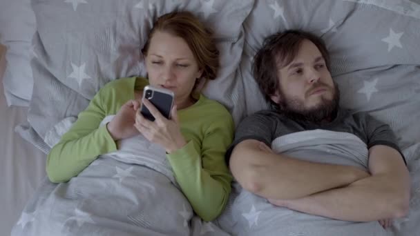 Caucasian Couple Fighting, arguing on Bed. Woman addicted to gadget - Smart Phone, ignoring Husband flirting in bed. Offended bearded Man lying turned back to his wife at night. - Filmagem, Vídeo