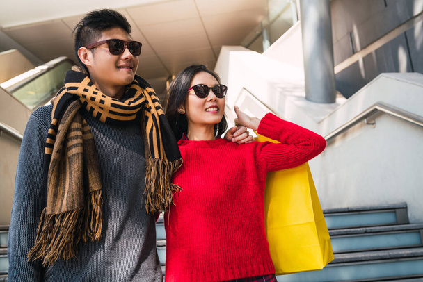 Renkli alışveriş torbaları taşıyan, alışverişin keyfini çıkaran, alışveriş merkezinde eğlenen güzel Asyalı çiftin portresi.. - Fotoğraf, Görsel