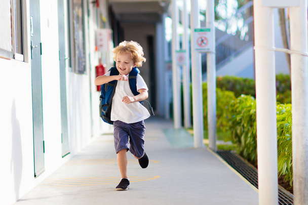 Dziecko idzie do szkoły. Chłopak biegający na szkolnym podwórku. Mały student podekscytowany powrotem do przedszkola lub przedszkola. Początek zajęć po wakacjach. Dzieci biegają do rodziców lub przyjaciół po lekcjach. - Zdjęcie, obraz