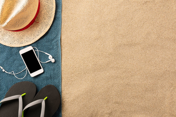 Летние каникулы композиция. Шляпа, смартфон и шлепанцы на песке. Жесткий свет с тенями. Летний фон. Состав границы из полотенца
 - Фото, изображение