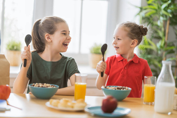 Happy children having breakfast. Kids eating cereal in kitchen. - Foto, afbeelding