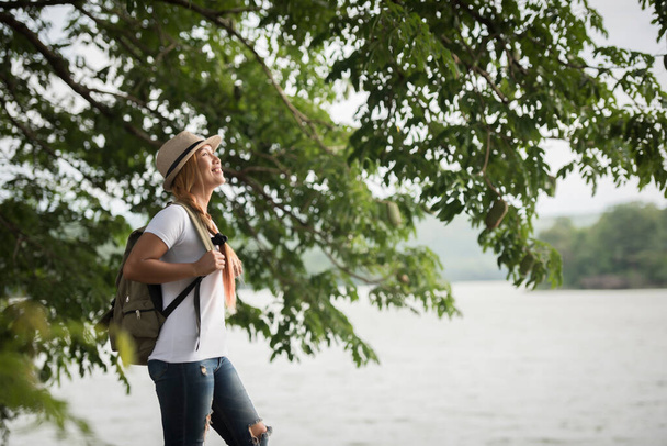 若い幸せな女性のバックパックは、川を探して立っている。女性旅行のコンセプト. - 写真・画像