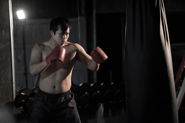 Porträt eines jungen asiatischen Mannes beim Boxen auf einem Boxsack im Fitnessstudio. - Foto, Bild