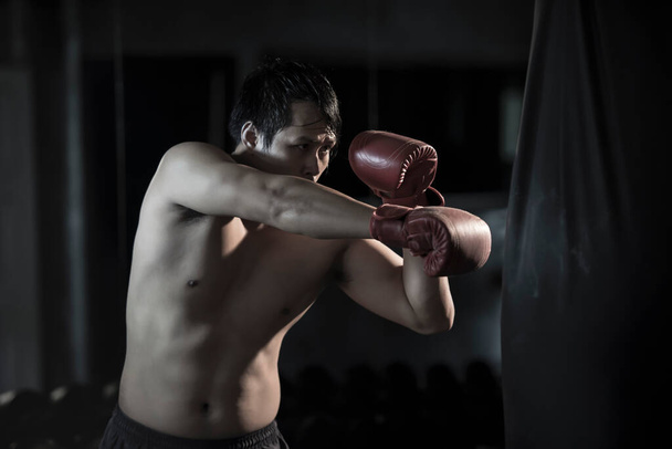 ジムでパンチングバッグの上でボクシングを練習している若いアジア人男性の肖像画. - 写真・画像