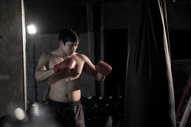 Portrait of a young asian man practicing boxing on a punching bag at gym. - Photo, Image
