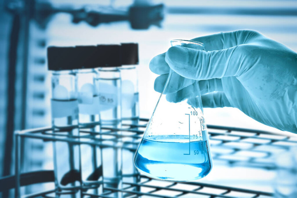 ręka naukowca trzymającego kolbę ze szkłem laboratoryjnym w chemicznym środowisku laboratoryjnym, koncepcja badań i rozwoju laboratorium naukowego  - Zdjęcie, obraz