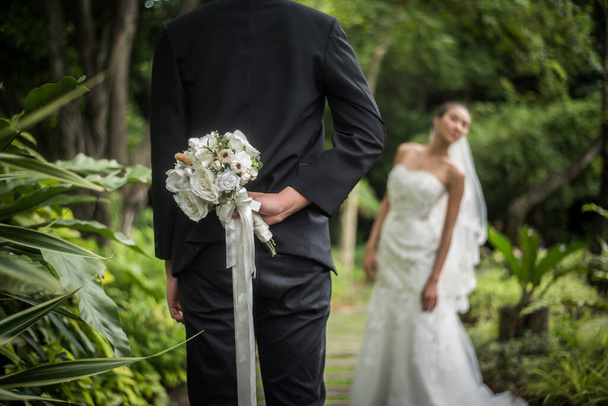 Porträt eines Bräutigams, der einen Blumenstrauß hinter seinem Rücken versteckt, um eine Braut zu überraschen. - Foto, Bild