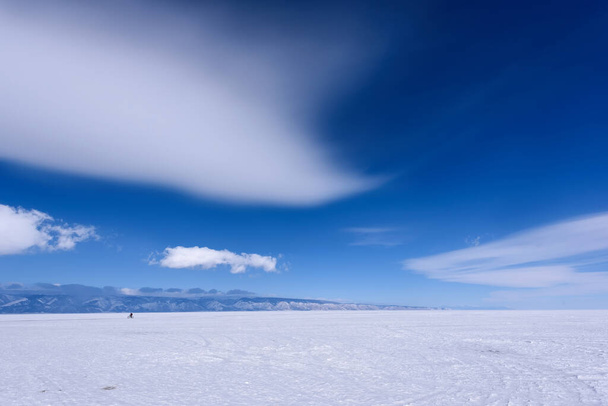 Silueta člověka jezdí na kole na zamrzlém jezeře Bajkal za slunečného počasí s krásnými mraky oblohy - Fotografie, Obrázek