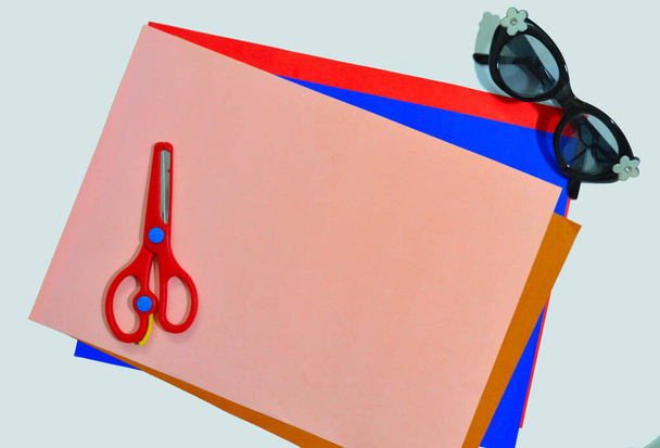 colour papers, scissors and specs on a white surface indicating a kid's activity desk - Photo, Image