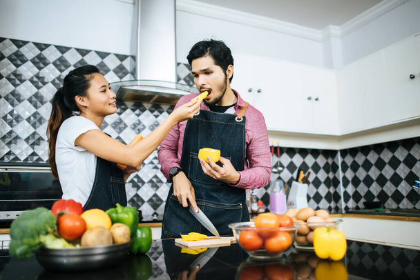 feliz jovem casal ajudar uns aos outros cortando vegetais se preparando para cozinhar na cozinha em casa
. - Foto, Imagem