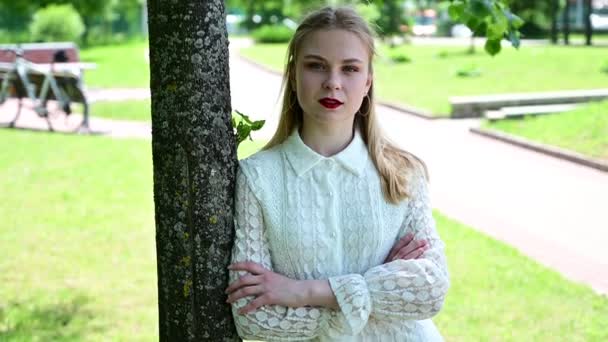 Video portret van een blond meisje staan kijken recht in het park. - Video
