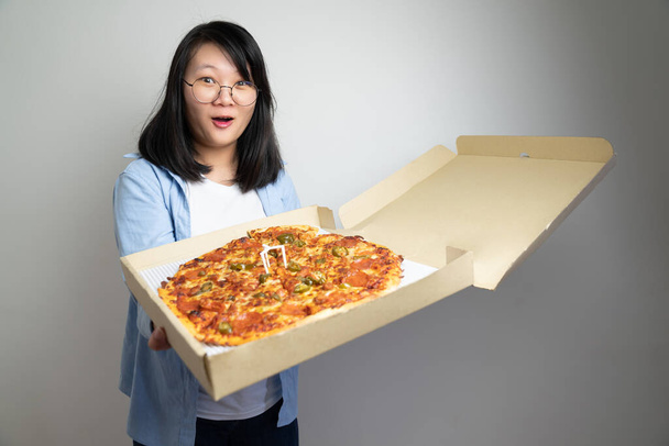 Aziatische bril jonge vrouw opent Pizza Box en windt zich op over de grote formaat pizza erin. Opname in studio licht. - Foto, afbeelding