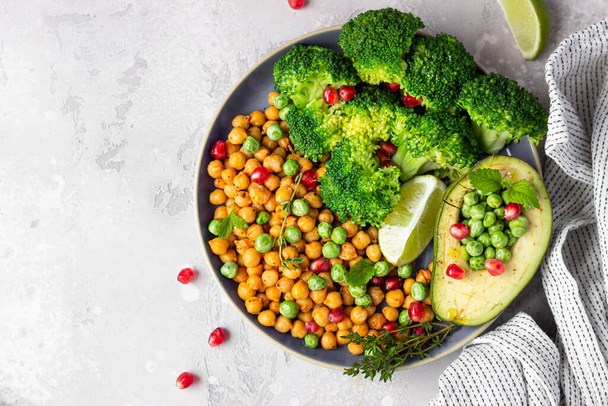 Healthy vegetable lunch of broccoli, roasted chickpeas, avocado, green peas, pomegranate seeds, lime and mint on a plate. Vegan food, clean eating or dieting concept. Top view. - Fotoğraf, Görsel