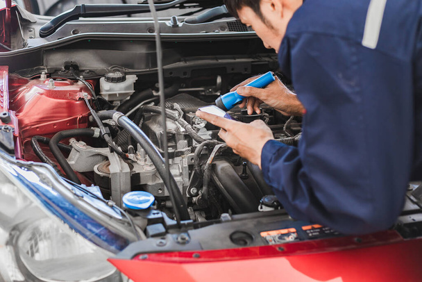 Asian Man mechanik inspekcja Shine silnik pochodni sprawdzanie błędów w silniku z aplikacji smartphone.Red samochód do ubezpieczenia serwisowego z silnikiem samochodowym. do transportu samochodowego - Zdjęcie, obraz