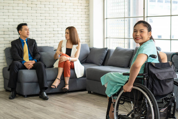 молода азіатка з інвалідністю зі усміхненим обличчям сидить у інвалідному візку, розмовляючи зі своїми друзями на робочому офісі. інвалідність та концепція інвалідності
 - Фото, зображення