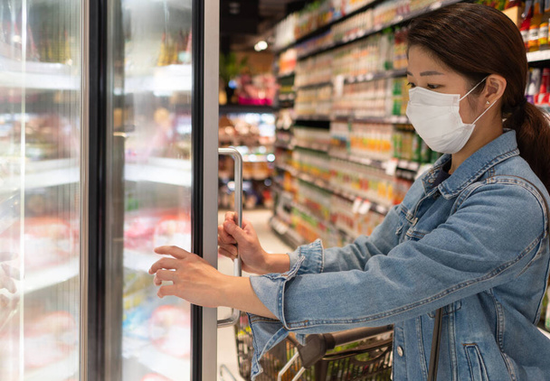 joven mujer asiática con máscara y mantener distanciamiento social mientras compra comida en el supermercado. nuevo concepto normal, covid-10 y coronavirus
 - Foto, Imagen