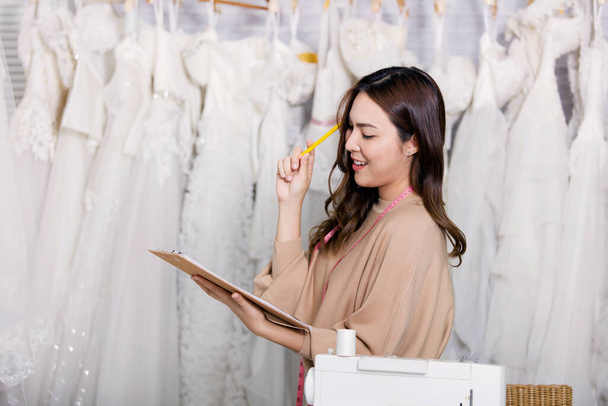 A női tervező mosollyal az arcán áll, jegyzeteit ceruzával írja az írótáblára egy ruhaboltban. Üzlettulajdonosok áll egy butikban ruhák a háttérben. - Fotó, kép