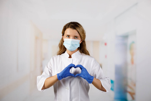 Woman with a medical mask and hands in latex glove shows the symbol of the heart. Doctor for the heart. Love to our pancreas. Love our medical professionals. - Foto, afbeelding