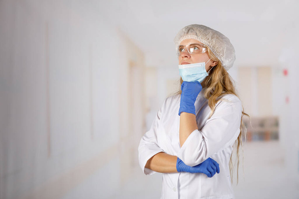 Доктор женщина в защитном костюме задумчиво стоит в коридоре больницы. Коронавирусная инфекция опасна для жизни
 - Фото, изображение