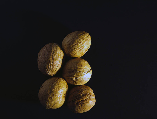 A pile of walnuts on a black background with dim light - Photo, image