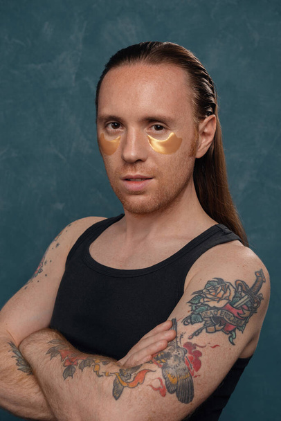 Retrato de un hombre con tatuajes y pelo largo con manchas bajo los ojos
. - Foto, imagen