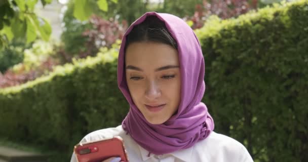 Mooie jonge vrouw kijkt naar smartphone, het dragen van traditionele hoofddoek. Aantrekkelijk vrouwtje in hijab - Video