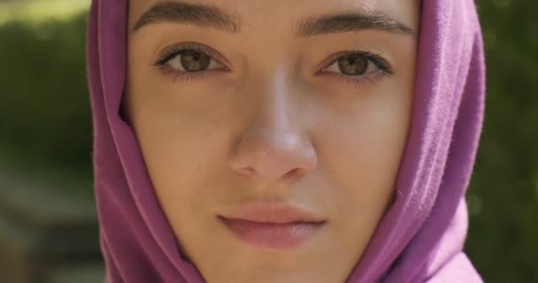 Mooie jonge vrouw die naar de camera kijkt en een traditionele hoofddoek draagt. Aantrekkelijk vrouwtje in hijab. Sluiten. - Video