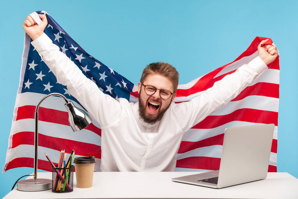 アメリカの国旗を掲揚し、職場でクレイジーな喜びを叫び、労働者の日や米国独立4日目の7月、政府の雇用支援を祝う非常に幸せなビジネスマン。屋内隔離された - 写真・画像