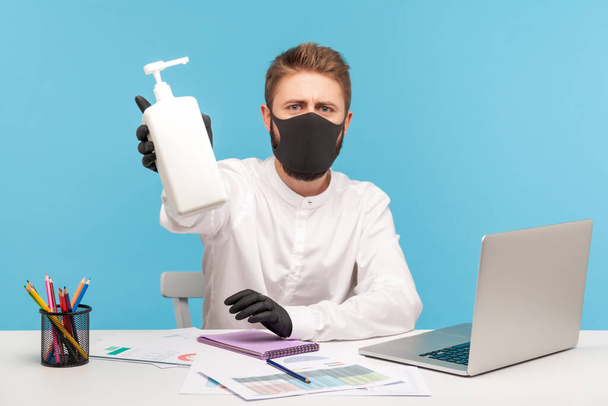 Man employee in hygienic face mask and gloves giving bottle with antiseptic gel, disinfection to prevent coronavirus at workplace, protection against contagious disease in office. studio shot isolated - Fotoğraf, Görsel