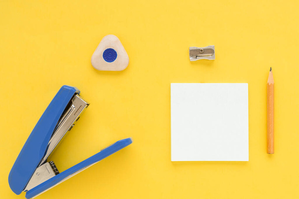 White square notes, pencil, eraser, blue stapler, sharpener on yellow paper backgroun - 写真・画像