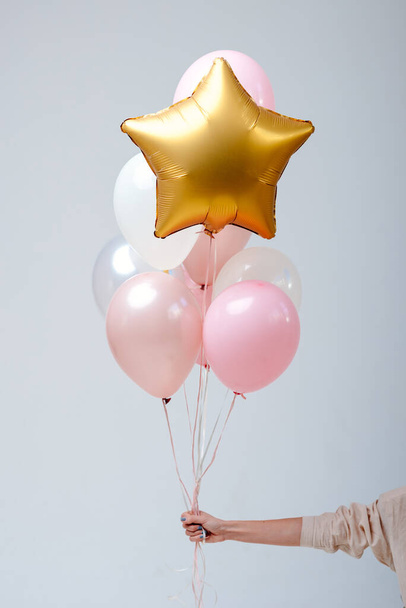 Composition of white, pink, transparent helium balloons and gold star in the hand of a woman on a white background. - Zdjęcie, obraz
