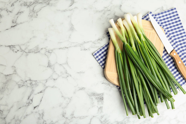 Fresh green spring onions, knife and cutting board on white marble table, flat lay. Space for text - Foto, Imagen